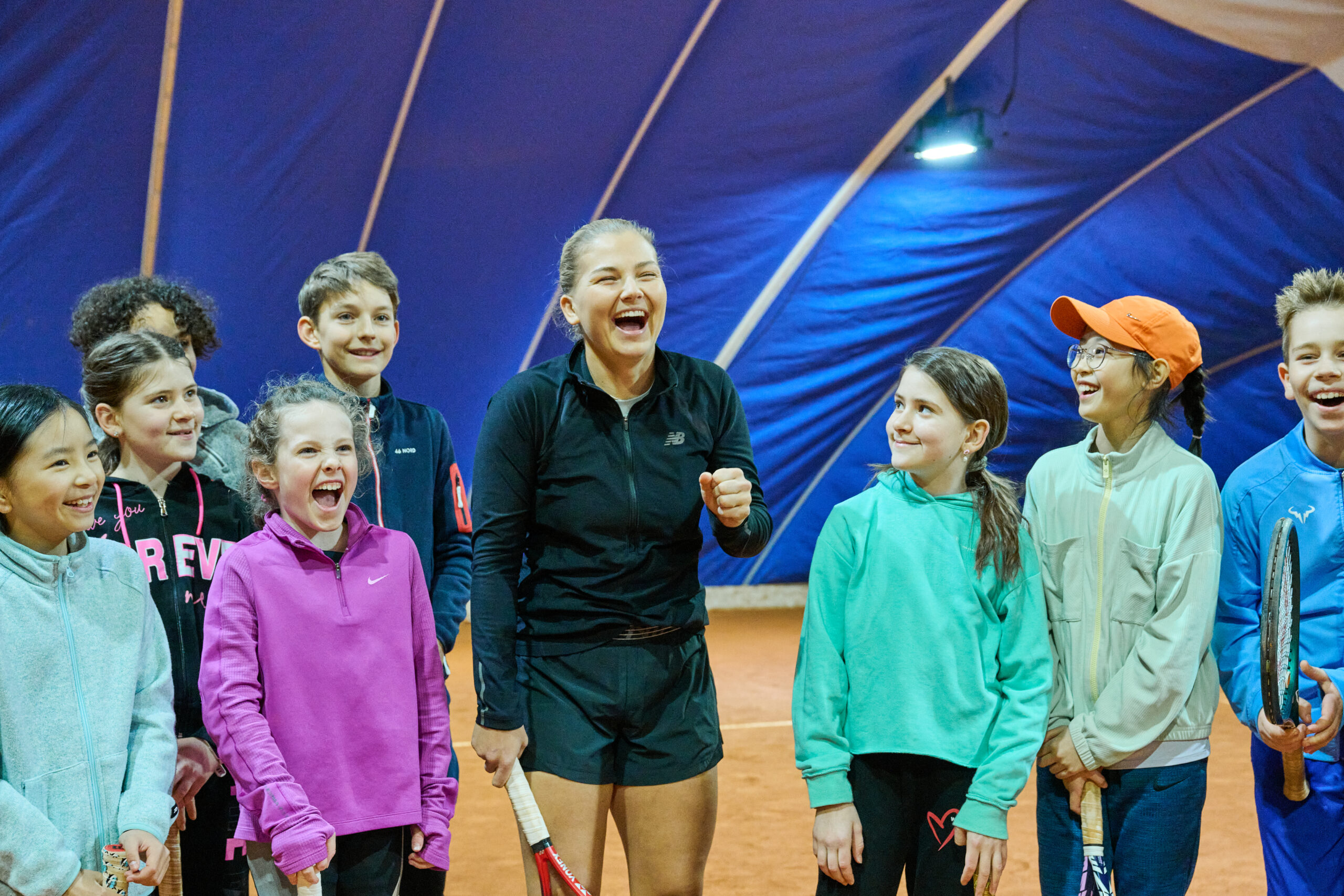 Links und recht von einer Tennispielerin stehen Kinder und schauen sie an
